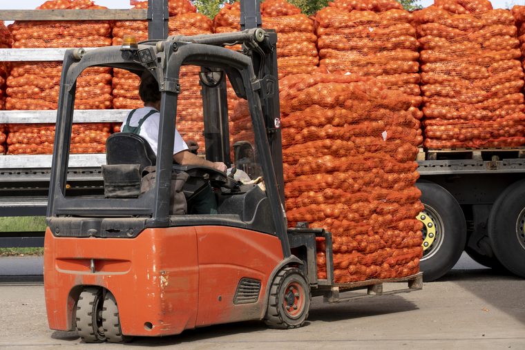 Forklift loading sacks of produce onto a flatbed truck at a depot
